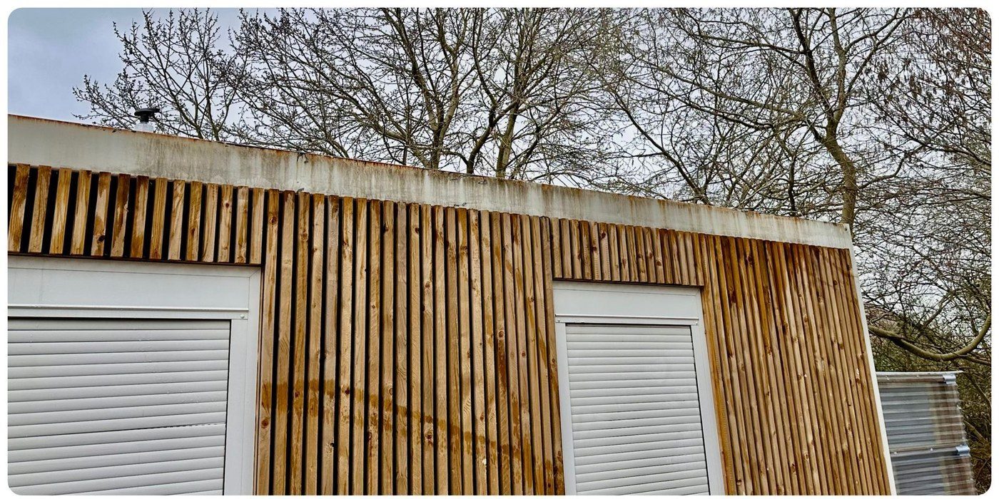 Timber-clad commercial building with green algae staining on upper fascia